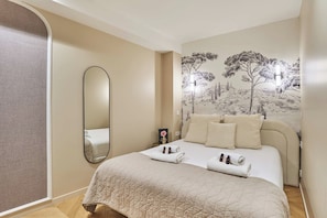 A neatly made bed with a quilted cover, a wall-mounted mirror, and a wall mural of trees. - Apartment AC Saint-germain des Pres Rue de Rennes (Paris)