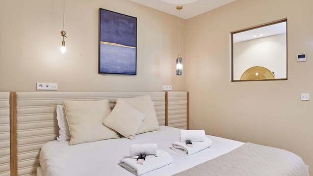 Una habitación de hotel con una cama, dos mesitas de noche, una obra de arte colgada en la pared, un espejo y un aplique de techo.