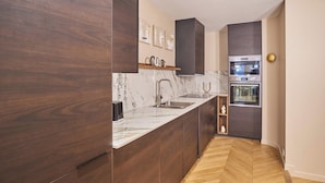 Una cocina moderna con armarios de madera oscura, encimera de mármol, horno empotrado y un lavamanos.