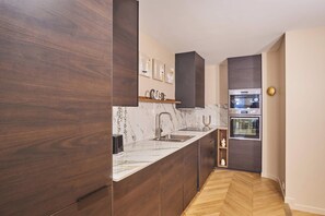Eine moderne Küche mit dunklen Holzschränken, einer Marmorarbeitsplatte, einem eingebauten Ofen und einem Spülbecken.
