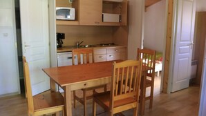 A compact kitchen with wooden cabinets, a microwave, and a sink. There is a dining table with chairs. - Chalet pet-friendly - 5 guests (Pleaux)