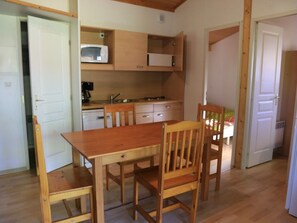 A compact kitchen with wooden cabinets, a microwave, and a sink. There is a dining table with chairs.
