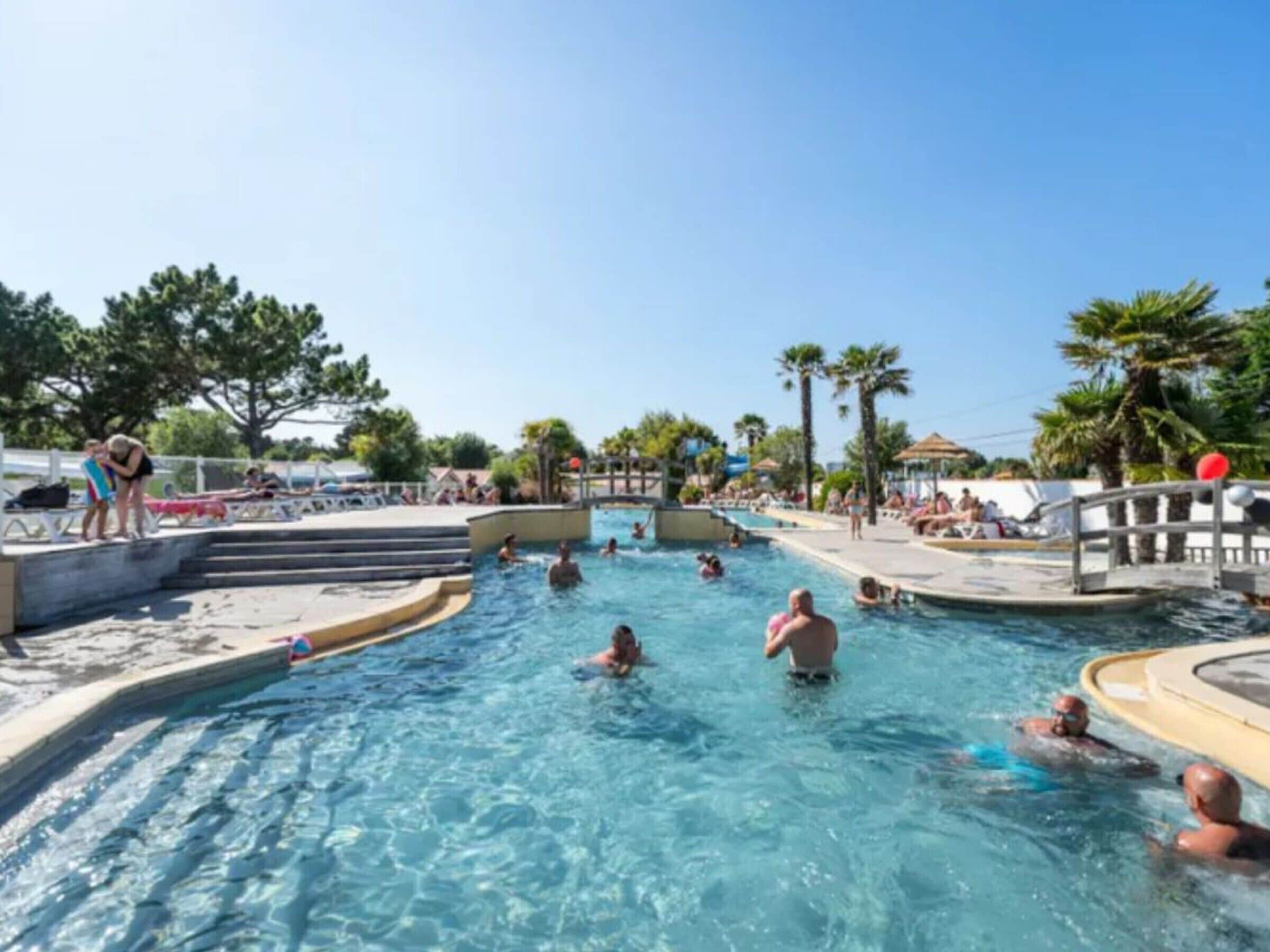 A swimming pool area with multiple pools, steps leading into the water, and people swimming.