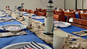 Ein Essbereich mit gedeckten Tischen, gestreifte Tischdecken, weiße Teller und eine dekorative Leuchtturm-Mitteldeoration.
