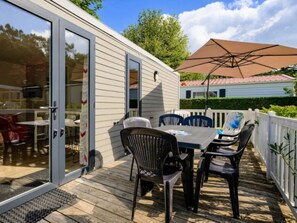 A covered deck with a table and chairs, a sliding glass door, and a white fence. - Mobile home 3 bedrooms, pets welcome - 6 guests (Saint-Jean-de-Monts)