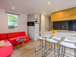 A modern kitchen with white bar stools, a red sofa, and a small table with a book. - Mobile home 3 bedrooms, pets welcome - 6 guests (Saint-Jean-de-Monts)