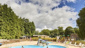 Piscina con tobogán, rodeada de sillas de descanso y una zona boscosa.