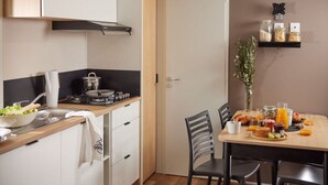 Una cocina compacta con estufa, lavamanos y armarios blancos. Hay una zona de comedor con una mesa dispuesta para el desayuno.