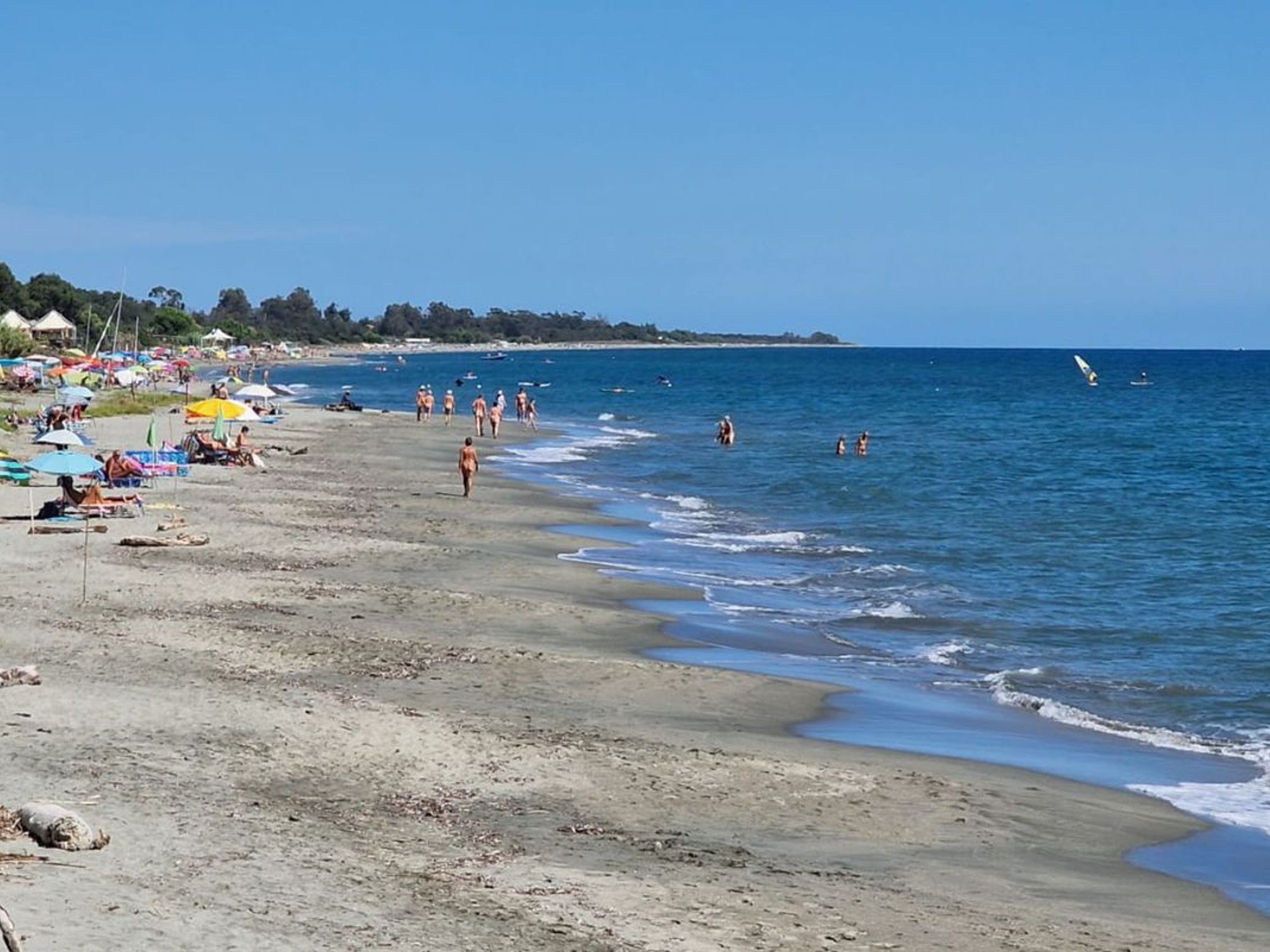 Una playa con gente tomando el sol y nadando, sombrillas y sillas de playa.