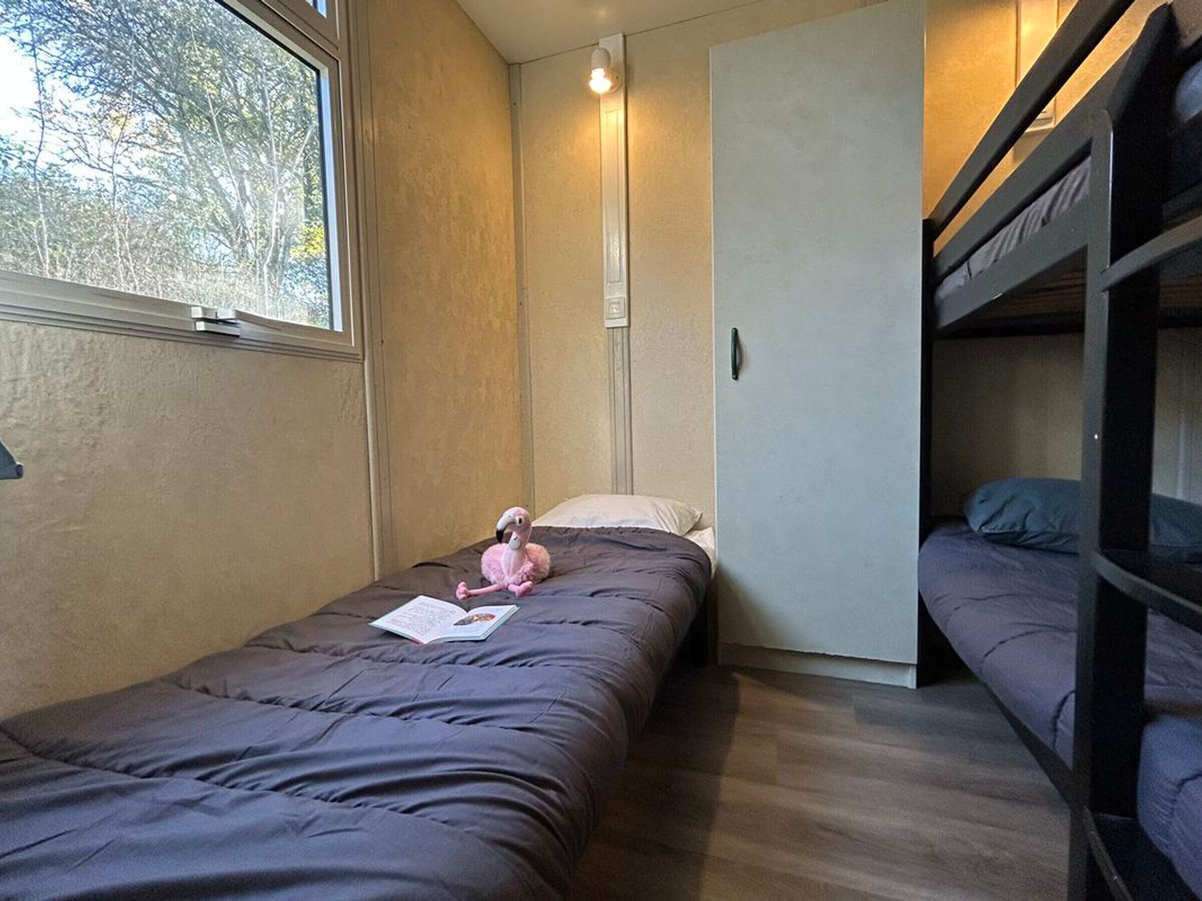 A compact room with a bunk bed, a single bed, and a window.
