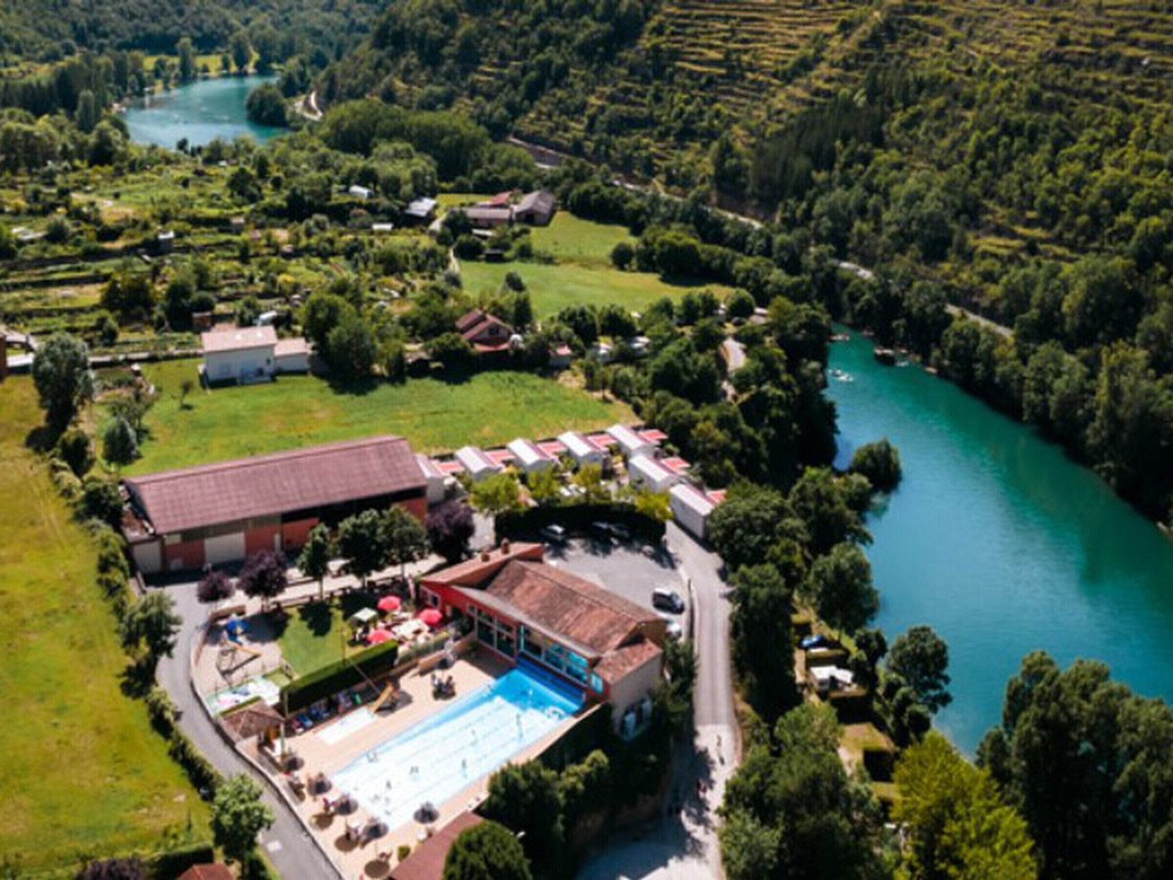 Vista aérea de un hotel con piscina, rodeado de follaje y un río.