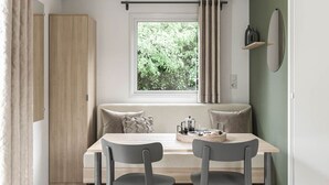 A dining area with a table, chairs, a window with curtains, a sofa, and a shelf with bottles. - Cozy mobile home, pets welcome - 2 guests (Saint-Rome-de-Tarn)