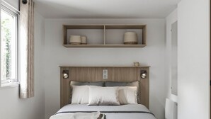 A bed with a wooden headboard, a bedside table, a shelf above the bed, and a window with curtains. - Cozy mobile home, pets welcome - 2 guests (Saint-Rome-de-Tarn)