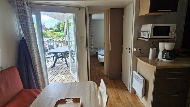Een knus kamertje met een bed, een kleine kitchenette, een zithoek met een tafel en stoelen, en een schuifdeur die leidt naar een terras.