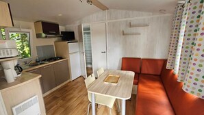 Een praktische keuken met een fornuis, magnetron en koelkast, een eettafel met stoelen, en een bank met een kleurrijk gordijn.