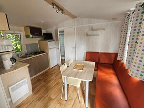 A compact kitchen with a stove, microwave, and refrigerator, a dining table with chairs, and a sofa with a colorful curtain.