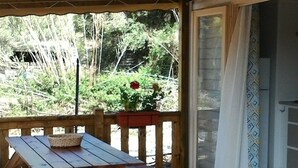Een houten terras met een picknicktafel en een mand, een houten omheining, en een uitzicht op groen en een gebouw op de achtergrond.