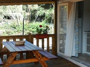 A wooden deck with a picnic table and a basket, a wooden fence, and a view of greenery and a building in the background. - Mobile home, pets allowed - 2 guests (Saint-Florent)