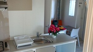 Een kleine keuken met een spoelbak, een klein aanrecht en een stoel.