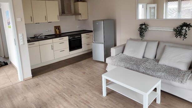 Een knus woongedeelte met een kitchenette, een witte bank en een bijzettafeltje.