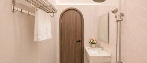 A bathroom with a wooden door, a towel rack, a sink with a vase of flowers, and a shower.