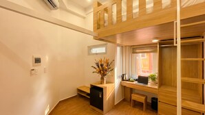 Une chambre compacte comprenant un lit superposé, un bureau avec un ordinateur portable, un petit réfrigérateur, une fenêtre avec vue et une plante.