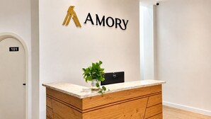 Un comptoir d’accueil agrémenté d’une plante, un meuble en bois et une enseigne murale portant le mot « AMORY ».