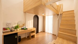 Une chambre d’hôtel moderne avec un bureau en bois, une petite cuisine équipée, un petit réfrigérateur, un miroir et un escalier.
