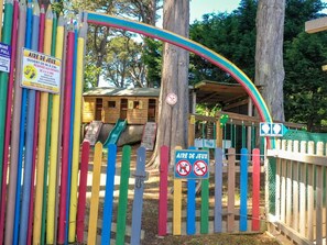 A playground with a rainbow arch, a wooden playhouse, and a sign indicating no dogs allowed. - Mobile home pets welcome - 4 guests (Perros-Guirec)