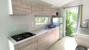 Een moderne keuken met een gasfornuis, magnetron, koelkast en een raam met uitzicht op groen.