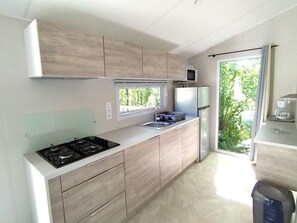 A modern kitchen with a gas stove, microwave, refrigerator, and a window with a view of greenery. - Mobile home, pets allowed - 4 guests (Chaillé-les-Marais)