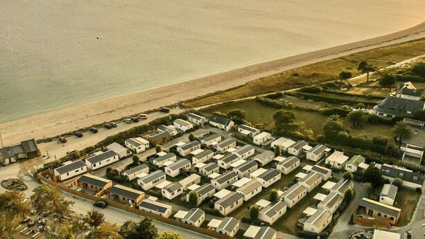 Parque de casas móviles costeras con filas de viviendas de una sola planta, una playa y vista despejada del océano.