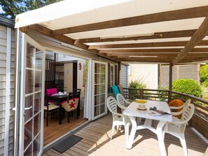 Un porche cubierto con mesa y sillas, una puerta corrediza de vidrio que da a un espacio interior y una terraza de madera.