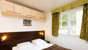 Une chambre à coucher avec un lit, une tête de lit en bois, des lampes fixées au mur, une fenêtre avec des rideaux et un tableau accroché au mur.