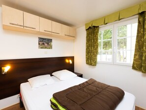A bedroom with a bed, wooden headboard, wall-mounted lights, a window with curtains, and a picture on the wall.