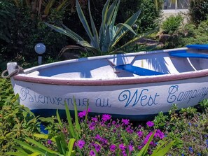 A boat with 'Bienvenue au West Camping' written on it, surrounded by greenery and flowers.