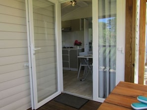 A room with a sliding glass door leading to a kitchen area, a small table with a pair of slippers, and a wooden floor. - Mobile home pets welcome - 2 guests (Saint-Florent)