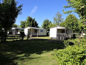 Two mobile homes with attached porches, surrounded by trees and grass.