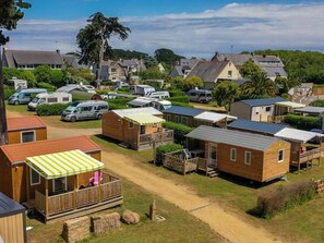 A campsite with mobile homes, a covered deck with chairs, and a dirt path. - Mobile home, pets welcome - 4 guests (Perros-Guirec)