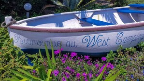 Ein Boot mit der Aufschrift 'Bienvenue au West Camping', umgeben von Grünpflanzen und Blumen.