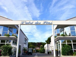 Entrada d'un edifici amb un rètol que diu 'L'Abri des Pins' i un vehicle estacionat al davant.