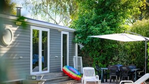 Een klein huis met een terras, een witte stoel, een tafel en een parasol.