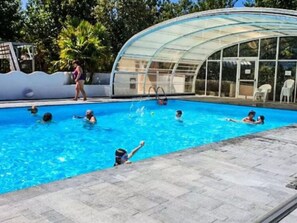 Ein Schwimmbecken mit Glasveranda, umgeben von einer gepflasterten Terrasse.