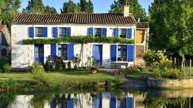 Ein zweistöckiges Haus mit blauen Fensterläden und einem Garten mit Teich.