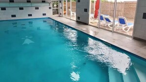 Una piscina interna con pareti di vetro trasparenti, pavimento piastrellato e struttura del soffitto in legno.