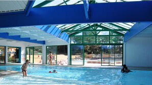 Una piscina interior con paredes de vidrio transparente, techo azul y zona de piscina visible a través del vidrio.