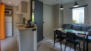 Een kleine keuken met een gasfornuis, magnetron en oven, een eethoek met een tafel en stoelen, en een raam met uitzicht.
