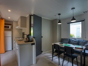 A compact kitchen with a gas stove, microwave, and oven, a dining area with a table and chairs, and a window with a view. - Mobile home, pets allowed - 10 guests (Groléjac)