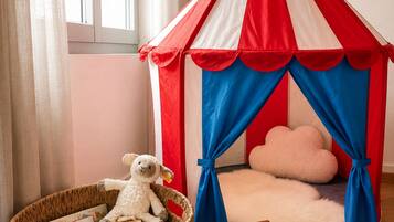 Une tente de jeu pour enfants, avec un tissu rayé rouge et blanc et des rideaux bleus, un jouet en peluche, un panier rempli de livres et une petite chaise en bois.