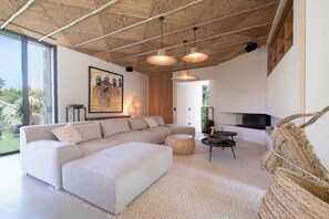 A modern living room with a large sectional sofa, a round coffee table, and a TV mounted on the wall. - Prestige Villa a/c 12P With Pool & Lounge (Ramatuelle)
